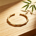 Gold bracelet on a wooden surface with a bamboo leaf